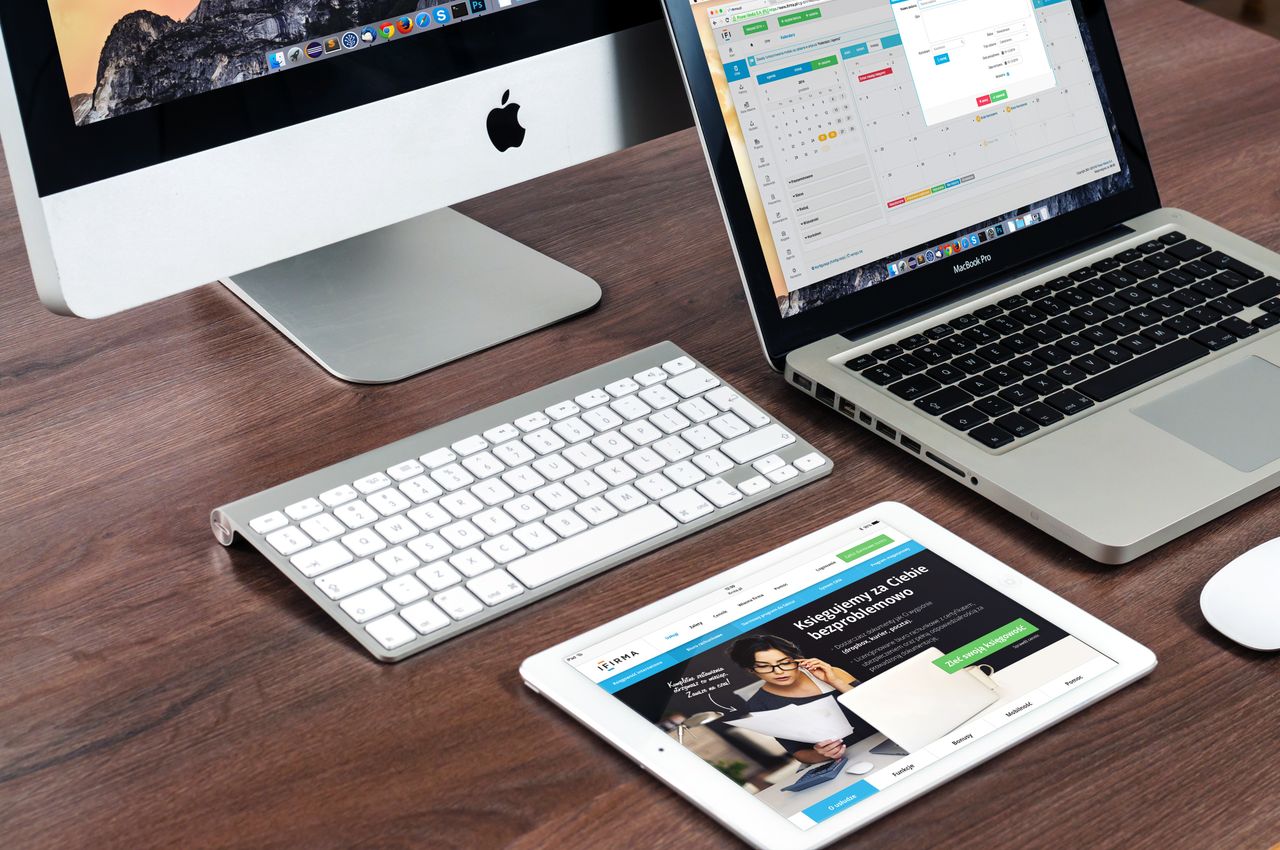 about-us-02 A sleek office desk setup featuring Apple devices: iMac, MacBook, and iPad.